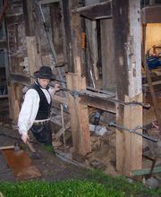 Zimmermann bei der Restaurierung eines alten Fachwerkhauses, umgeben von Holz und Werkzeugen.