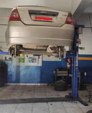 Carro prata suspenso em elevador de oficina mecânica. Equipamentos e pneus ao fundo.