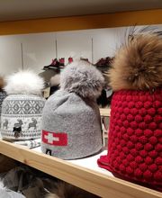 Verschiedene bunte Wintermützen mit Fellbommel auf einem Regal präsentiert.