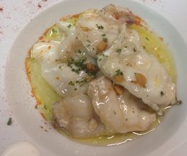 Plato de pescado en salsa con hierbas y piñones, decorado con gotas de crema en el borde.