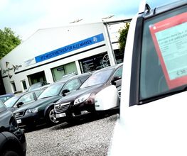Autohandel mit mehreren Pkw, Preisschild sichtbar, Werkstatt im Hintergrund.