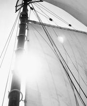 Schwarz-Weiß-Foto von Segel und Mast eines Bootes, mit sonnigem Himmel im Hintergrund.