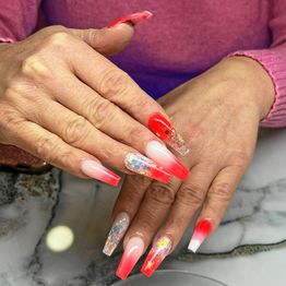 Frau mit langen, rot-pinken Gelnägeln und Glitzer verziert, trägt einen rosa Pullover.