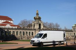 Weißer Lieferwagen vor einem historischen Gebäude mit einer goldenen Krone auf dem Dach.