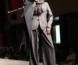 Frau auf Modenschau trägt Anzug mit Mantel, Sonnenbrille und modischem Schal.