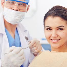 Dentist wearing mask and patient smiling during dental check-up.
