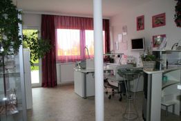 Heller Raum mit Behandlungstischen, Pflanzen und roten Vorhängen, geeignet für kosmetische Anwendungen.