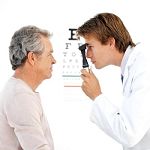 Doctor examining an older man's eyes with an eye chart in the background.
