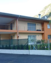 Zweistöckiges orangefarbenes Haus mit Balkon, Gartenzaun und Palme im Vordergrund.