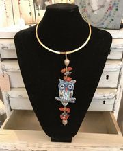 Goldene Halskette mit Eulenanhänger und roten Akzenten an schwarzer Büste ausgestellt.