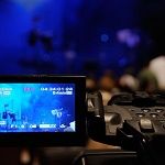Camera capturing a dimly lit stage with performers, shown on its display screen.