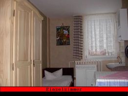 Einzelzimmer mit Bett, Schrank, Waschbecken und Fenster mit Vorhängen.