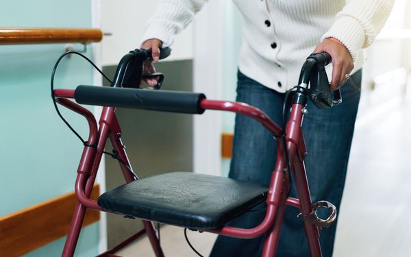 Person geht mithilfe eines Rollators einen Krankenhausflur entlang.
