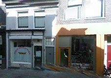 Twee winkels naast elkaar aan een straat, een met witte gevel en de ander met oranje omranding.