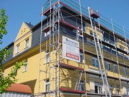 Gelbes Gebäude mit Gerüst für Renovierungsarbeiten, blauer Himmel im Hintergrund.