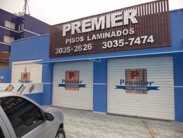 Fachada da loja Premier Pisos Laminados, com letreiros e portas azul e branca. Carro na frente.
