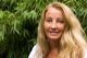 Eine lächelnde Frau mit blonden Haaren vor grünen Blättern.