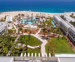 Vista aérea de un complejo hotelero frente al mar con piscinas y palmeras.