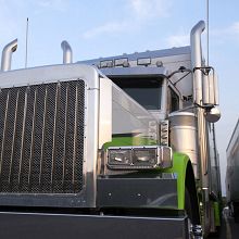 Close-up of a shiny green and silver semi-truck with a large grille under a clear sky.