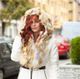 Woman in fur-lined hooded coat walking on a city street.
