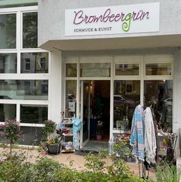 Außenansicht eines Kunsthandwerksladens mit Schildern. Vor dem Laden hängen bunte Tücher.