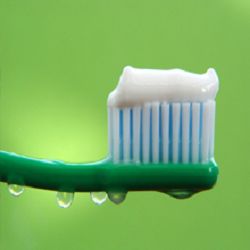 Toothbrush with toothpaste and water droplets on green background.