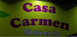Letrero amarillo con el texto "Casa Carmen Sidrería" en letras moradas y grises.