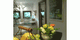 Ein Raum mit Obstkorb und Blumen, zwei Fenster im Hintergrund, helle und freundliche Atmosphäre.