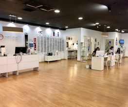Óptica moderna con mostradores, gafas expuestas y dos personas trabajando en mesas.