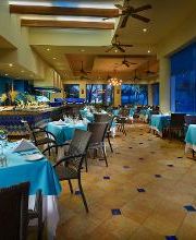 Restaurante elegante con mesas con manteles turquesa y luces cálidas. Ventanas grandes a la derecha.