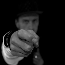 Verschwommener Mann zeigt mit ausgestrecktem Finger auf die Kamera, schwarzer Hintergrund.