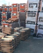 Pacchi di tegole e materiali edili impilati su pallet all'aperto.