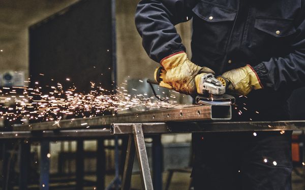 Schlosser bearbeitet einen hohlen Metallpfahl mithilfe einer Schleifmaschine. Funken sprühen während dieser Arbeit.