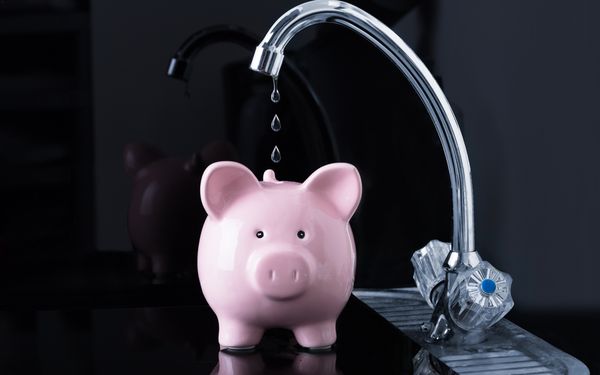 Wasser tropft aus einem Wasserhahn in ein Sparschwein hinein. Dies soll das Einsparen von Kosten beim Wasserverbrauch darstellen.