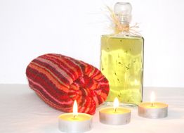 Rotes Handtuch, Flasche mit Öl und drei brennende Teelichter auf weißem Hintergrund.