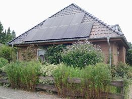 Backsteinhaus mit Solarpaneelen auf dem Dach, umgeben von einem Garten mit verschiedenen Pflanzen.