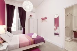 Habitación elegante con cama matrimonial, decoración en tonos morados y baño adjunto.