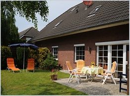 Ein Garten mit Liegestühlen, Tisch, Stühlen und Sonnenschirm vor einem roten Ziegelhaus.