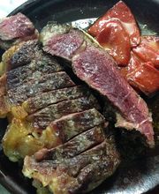 Carne asada en rodajas, con trozos de tomate rojo a un lado, servida en un plato negro.