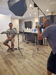 Photographer taking a picture in a studio with a seated person, lights, and equipment.