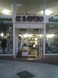 Fachada de una tienda con letrero "El Rastro", interior iluminado y puerta de entrada abierta.