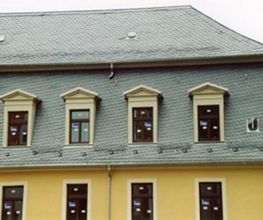 Historisches Gebäude mit Schieferdach und gelber Fassade, Fenster mit dekorativen Giebeln.