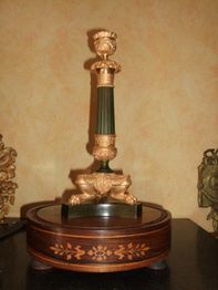 Dekorativer Kerzenhalter auf rundem Sockel mit goldenen Verzierungen, auf schwarzem Tisch.