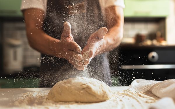 Bäcker bestäubt eine Arbeitsfläche mit Mehl, damit er dort den Teig vorbereiten und ausrollen kann.