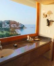 Habitación con lavabo, vista al mar y colinas desde una ventana grande.