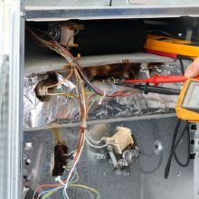 Technician using a multimeter to check wiring inside an electrical panel.