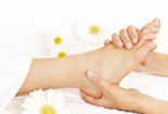 Massage einer Fußsohle mit weißen Blüten im Hintergrund.