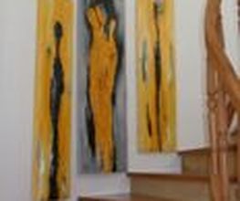 Drei abstrakte Gemälde in Gelb und Schwarz hängen an einer Wand neben einer Holztreppe.
