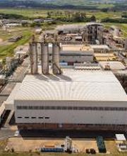 Vista aérea de uma fábrica grande com várias estruturas e áreas verdes ao redor.