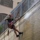 Man in safety harness power washing tall brick building.